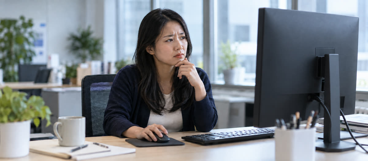 An IT administrator at her office desk rests her chin on her hand and frowns, hesitating over what she sees on her monitor.